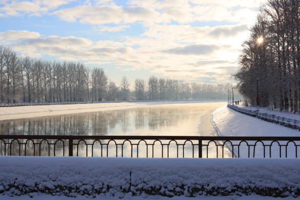 A beautifully serene winter scene featuring a snowcovered river elegantly flanked by bare trees beneath a cloudy sky