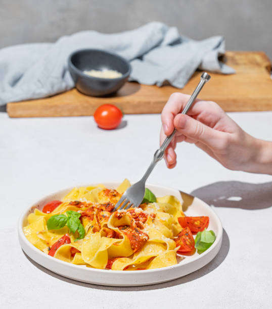 istock Hand holding fork with tagliatelle or pappardelle pasta with tomato sauce, basil and parmesan cheese in plate 2192927714