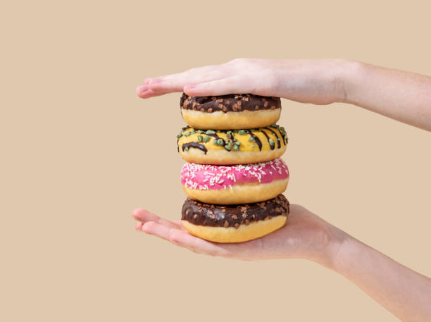 istock Hands holding stack of glazed donuts with different toppings on beige background. 2192927991
