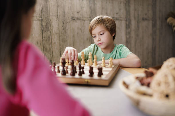 Cute boy playing chess game whit his female friend at home