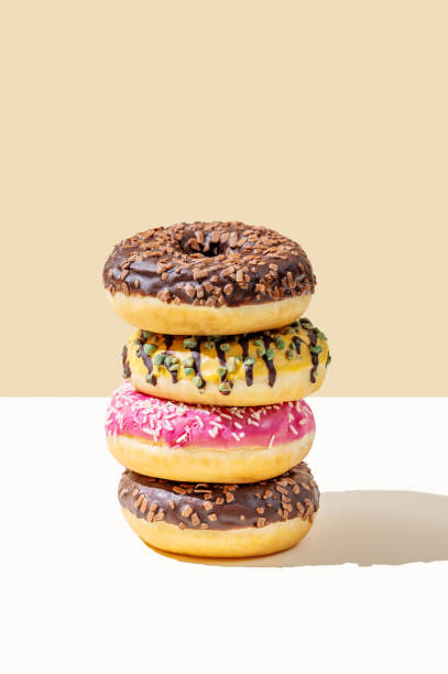 Stack of glazed donuts with different toppings on beige and white minimalistic background.