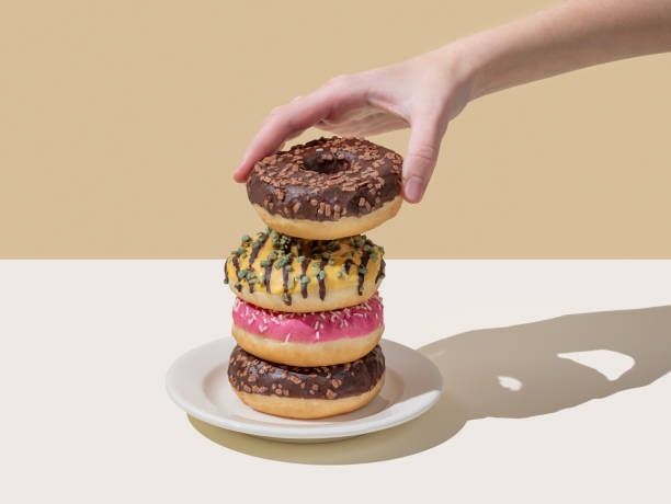 istock Hand takes one donut from stack of glazed donuts with different toppings on beige and white background. 2192928330