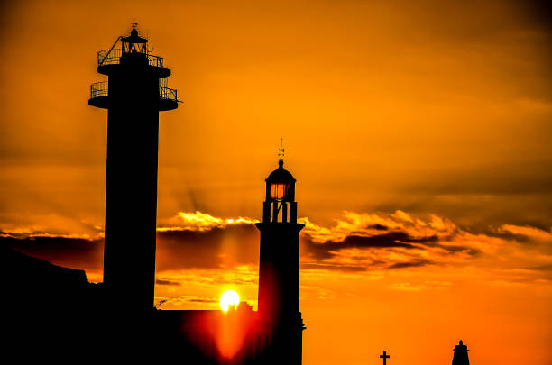 istock A lighthouse and a church tower are silhouetted against a sunset 2192929291
