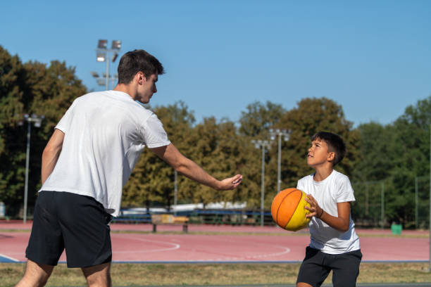 istock Outdoor basketball training for kids, featuring a coach teaching a young boy shooting technique. Focus on skill building, precision, and fostering youth development in sports. 2192935953
