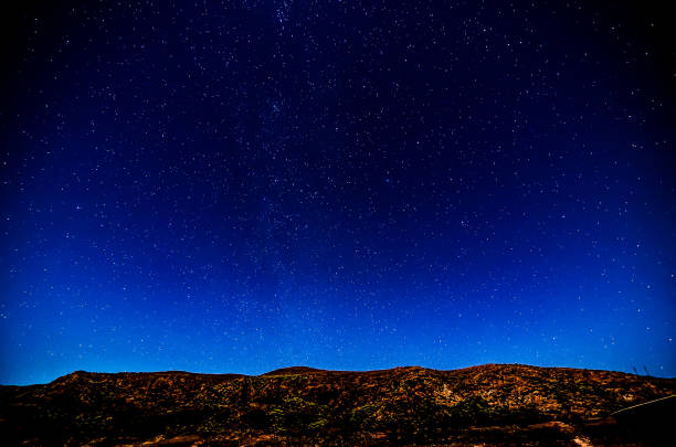 A dark sky with a few stars and a mountain in the background. The sky is clear and the stars are shining brightly
