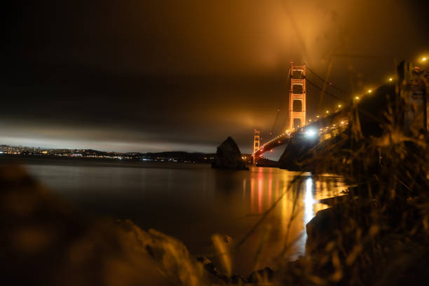 Low cloud obscuring the tops of the Golden Gate Bridge in California, illuminated as dusk approaches, with a long exposure blurring the sea.