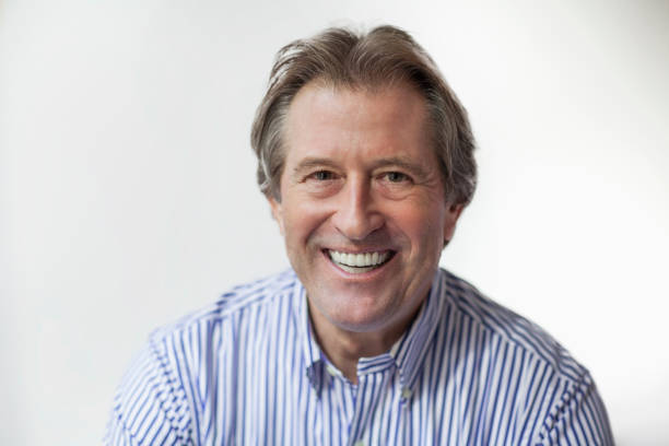 Happy man standing in front of an American flag. He is wearing a grey jacket, yellow shirt, and an \