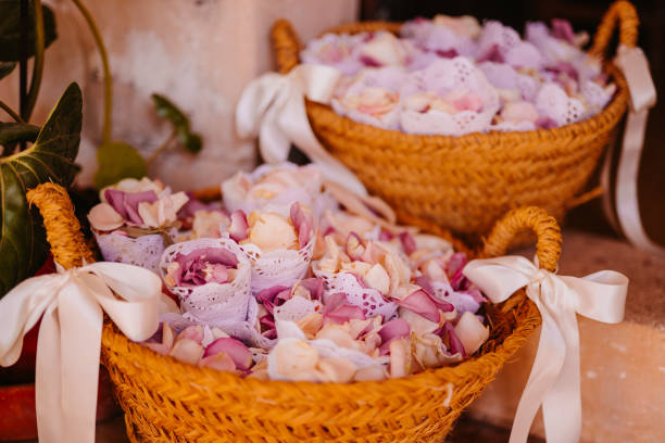 Two large wicker baskets adorned with elegant white silk ribbon placed on a staircase and filled with small pouches of beige and soft lilac rose petals  ready for tossing during a wedding celebration. Color editing. Part of a wedding series.