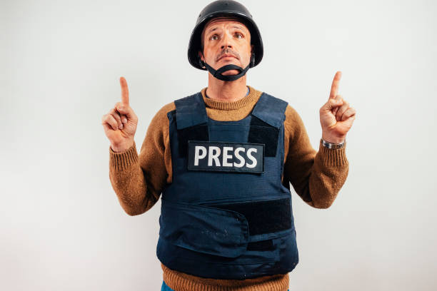 Reporter in bulletproof vest pointing to the sky.