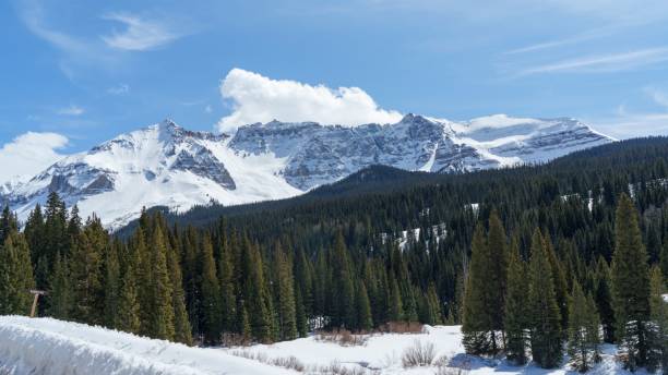 istock Snow-covered mountains and evergreen forests under a blue sky. 2192964302