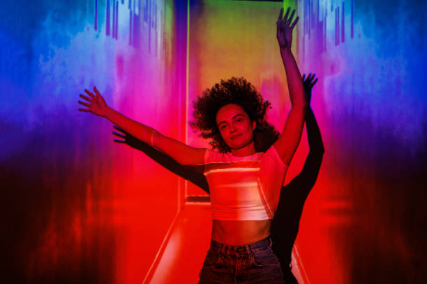 istock Woman joyfully posing with arms raised under vibrant colorful lights 2192965315
