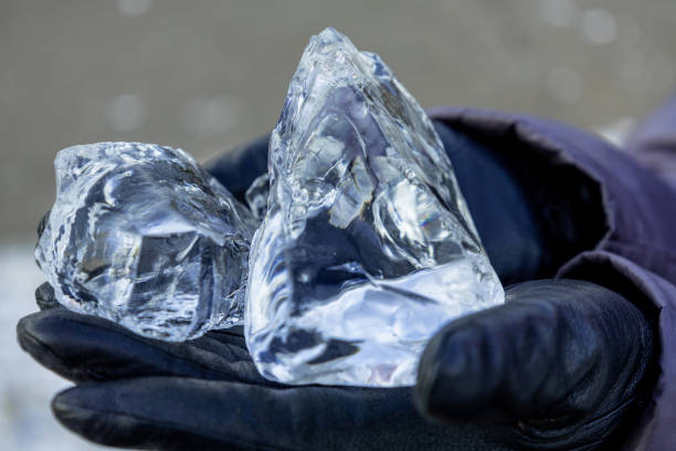 Large clear ice cubes rest in a gloved hand, highlighting their sharp edges and transparency against a winter backdrop. The scene conveys a sense of cold weather and natural beauty.