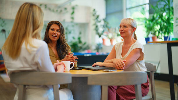 A group of professional businesswomen enjoying a relaxed conversation during their break time. Set in a green office with abundant natural light and vibrant plants, the scene emphasizes a balance between work and leisure in a collaborative and sustainable environment.