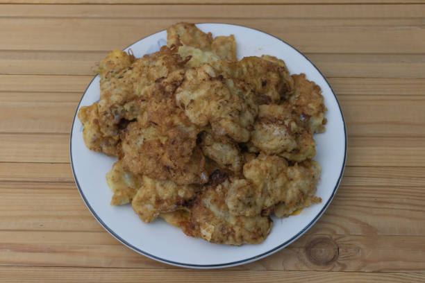 Deep-fried chicken skin fritters on a white plate, top view, on a wooden table background.