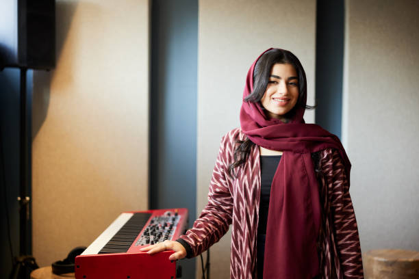 In traditional Middle Eastern clothes, the woman stands beside a piano synthesizer.