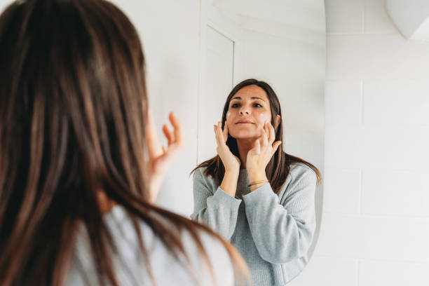 istock Woman applying face cream looking at mirror in bathroom 2192982970