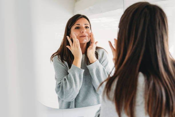 istock Woman applying moisturizer on her face looking in the mirror 2192983419