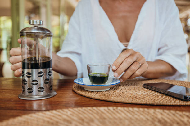 Woman Pouring Fresh Coffee from French Press at Cafe Table