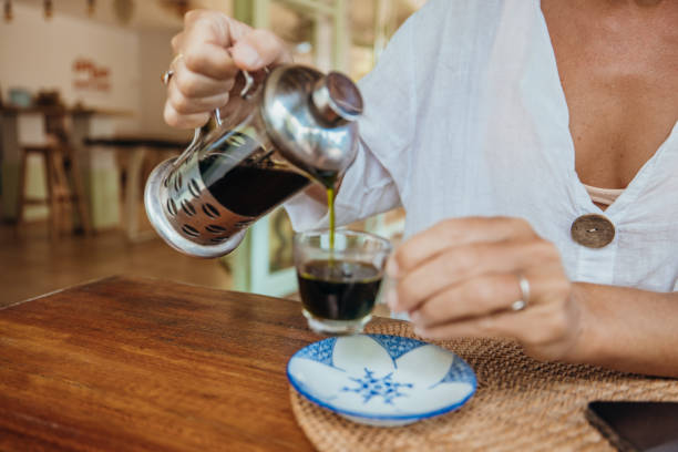 Woman Pouring Fresh Coffee from French Press at Cafe Table