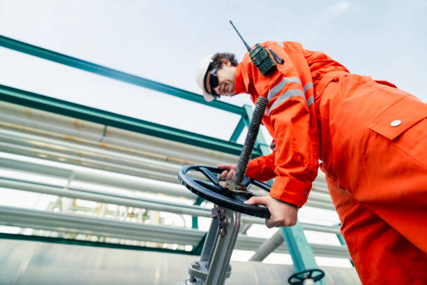 istock Engineer in bright orange safety suit adjusting industrial valve on a pipeline system, showcasing operational expertise, safety compliance, and technical skills in refinery operations. 2192988132