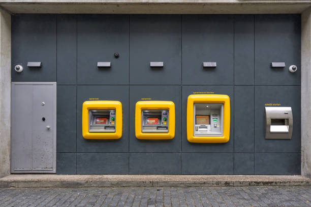 Three yellow atms and a night safe built in a gray wall with security cameras and a metal door