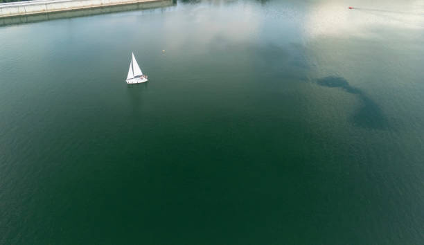 Aerial view of a sailboat gliding over tranquil green waters, creating a peaceful and serene scene that showcases the beauty of sailing and nature.