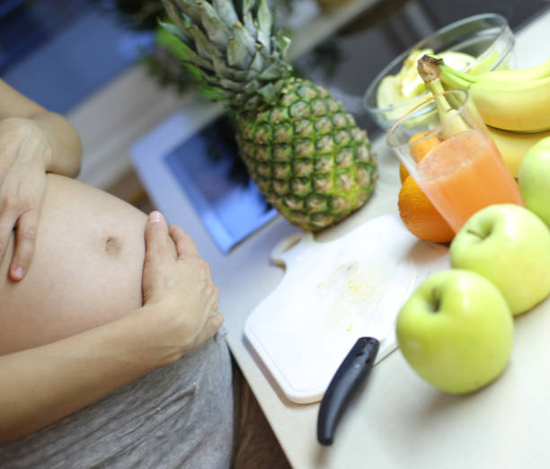 Smiling pregnant woman eating an apple and enjoying her morning in the bedroom.