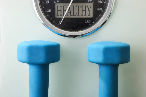 Two blue neoprene dumbbells on a white glass base of a scale with a health message display. Top view.