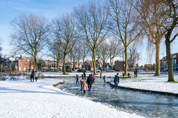 Dordrecht, Netherlands - February 14, 2021: Dutch families joyfully ice skating on a frozen canal in a picturesque park, embracing winter's charm and beauty of frozen waterways.