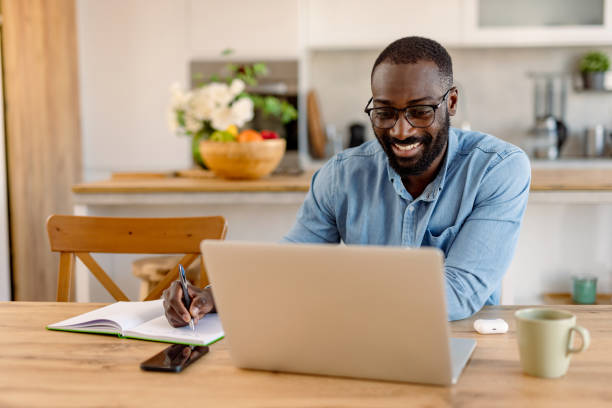 istock Happy man working from home taking notes looking at laptop 2193017317