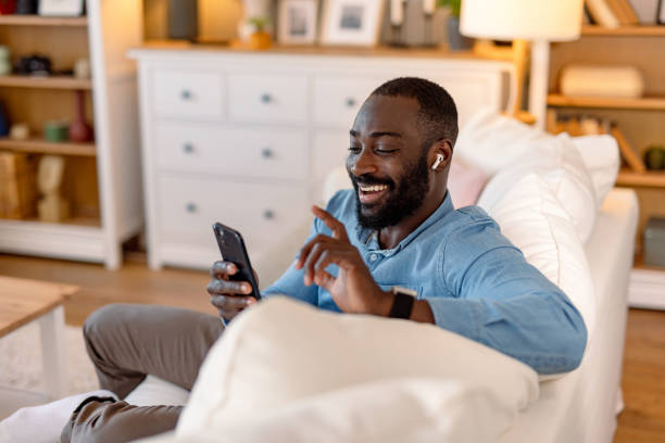 istock Young man using smartphone and wearing wireless earphones at home 2193017371
