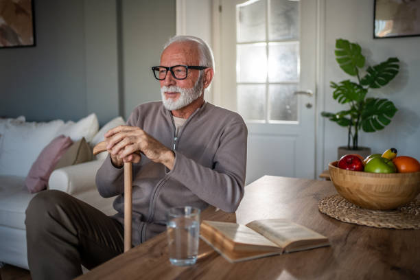 istock An elderly man relies on a walking stick for support, sits at a table, and spends his retirement days peacefully 2193021424