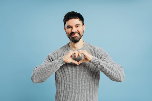 istock Smiling man making heart shape with hands on blue background 2193025511
