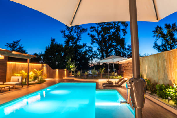 istock Elegant backyard pool view framed by an umbrella and serene evening sky. Modern outdoor retreat with warm lighting and stylish wooden design 2193033601
