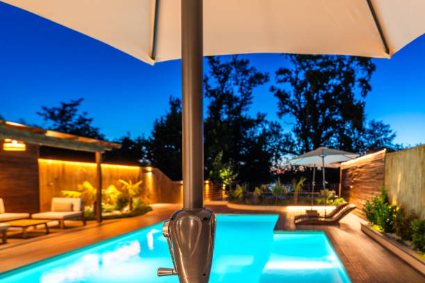 istock View of a luxurious backyard pool through a large umbrella under a twilight sky. Modern outdoor area with cozy lighting and sleek wooden decking 2193033609