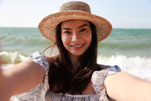 istock Pretty young woman with sun hat smiling and taking selfie on beach 2193034675