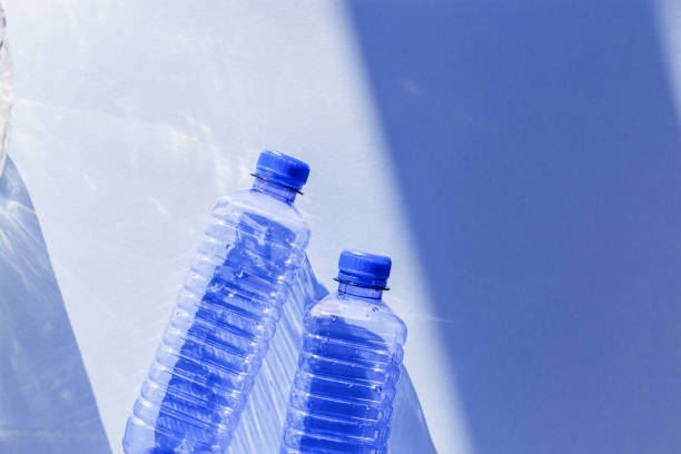 istock Transparent plastic bottles with blue caps and sun shadows on light background. Top view Water bottles at natural light. Themes of recycling, sustainability, water conservation, minimal style 2193036571