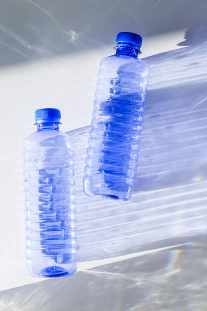 istock Blue plastic water bottles on white blue background with sunlight shadow and sun flare, Minimal top view photo, themes of ecology, recycling, sustainable living, reduce disposable plastics 2193036596