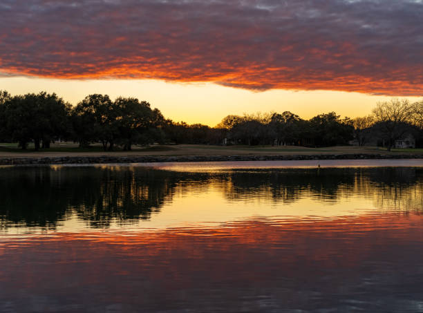 Dramatic sunset lighting a layer of clouds and reflected in the still water of Legacy Hills Park near Georgetown, Texas