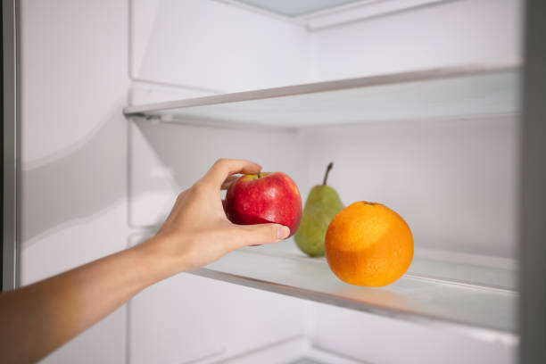 istock Hand picking up an apple from a refrigerator shelf with other fruits alongside. 2193053128