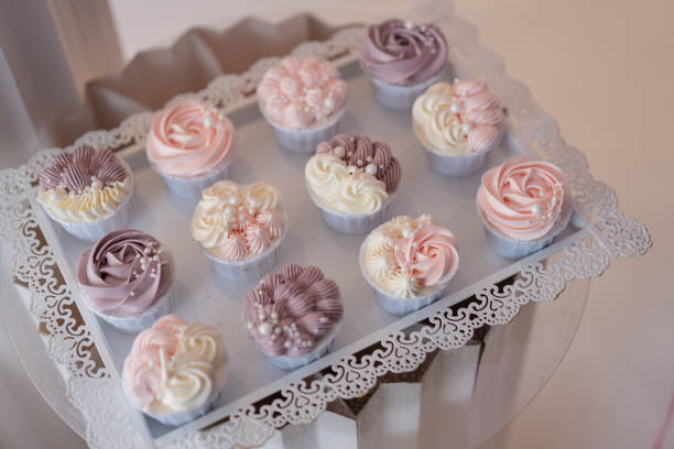 Cupcakes topped with pastel-colored flower-shaped cream decorations, arranged on a white tray. Birthday party concept.
