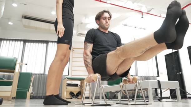 istock Client practicing seat leg lift on handles with instructor guidance. Habituate. 2193055123