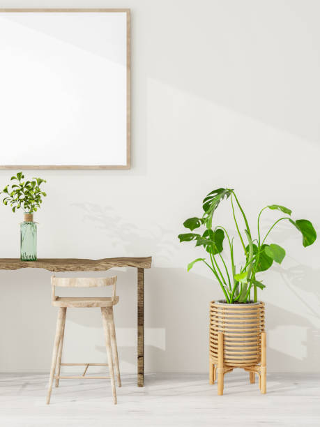 istock A minimalist interior scene featuring a rustic wooden table with two stools, a potted plant, and a blank picture frame on a light-colored wall. Vertical view. 2193055721