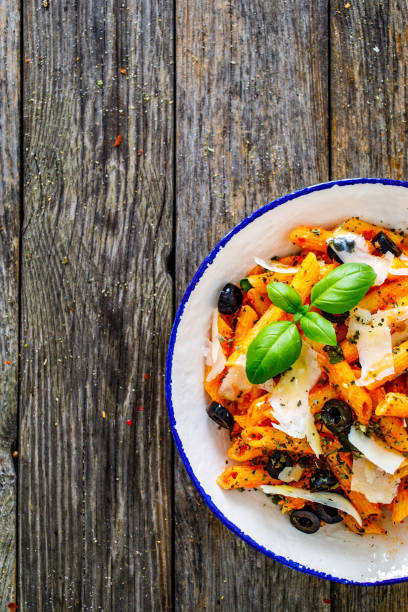 Noodles with pesto, parmesan cheese, basil and black olives served on wooden table