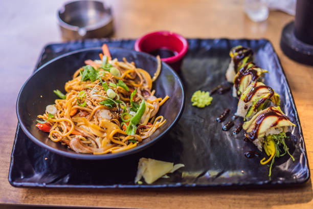 Asian noodles and sushi in black bowl.