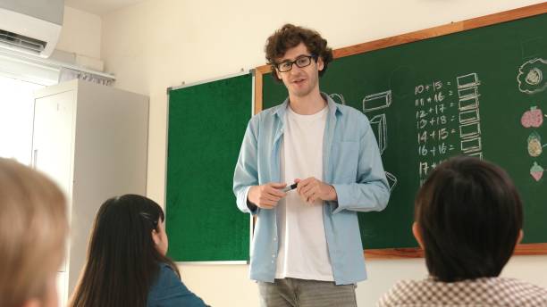 istock Mentor looking around classroom while standing in front of blackboard. Pedagogy. 2193060142