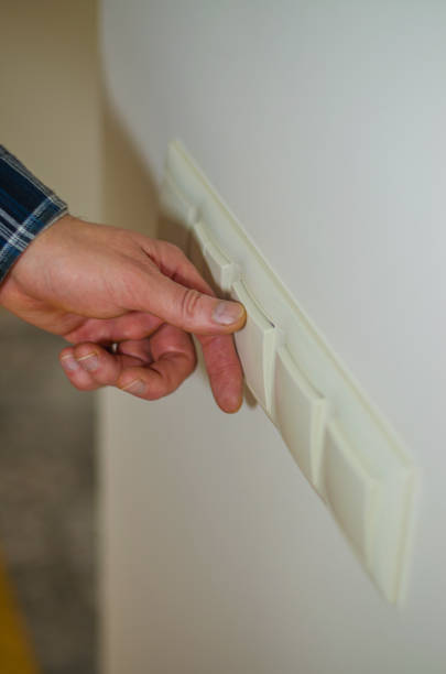 istock A man's hand reaches out to flip a light switch on a white wall 2193062791