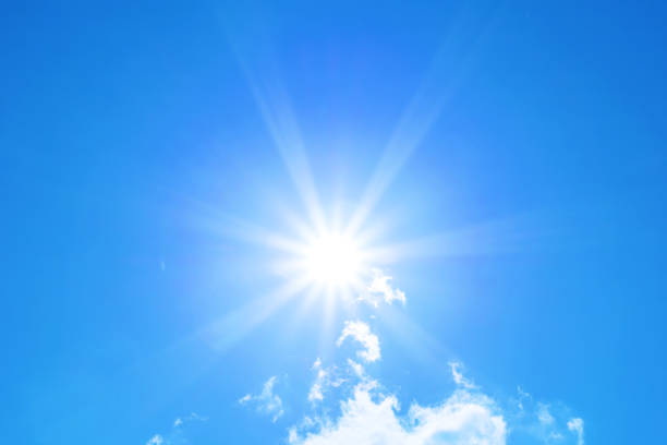 Bright sun with beautiful beams on a blue sky with light clouds. Space for copy.