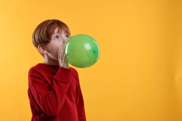 istock Boy inflating green balloon on orange background, space for text 2193066577