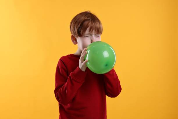 istock Boy inflating green balloon on orange background 2193066609